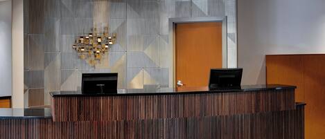 A reception desk with a modern design, featuring a geometric patterned wall and a wooden panel.