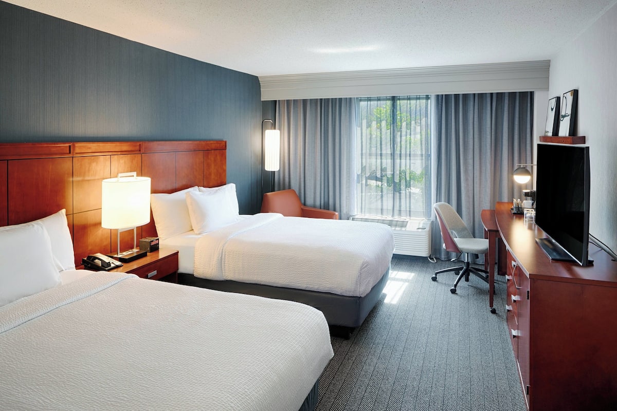 A hotel room with two beds, a desk, a chair, a TV, and a window with curtains.