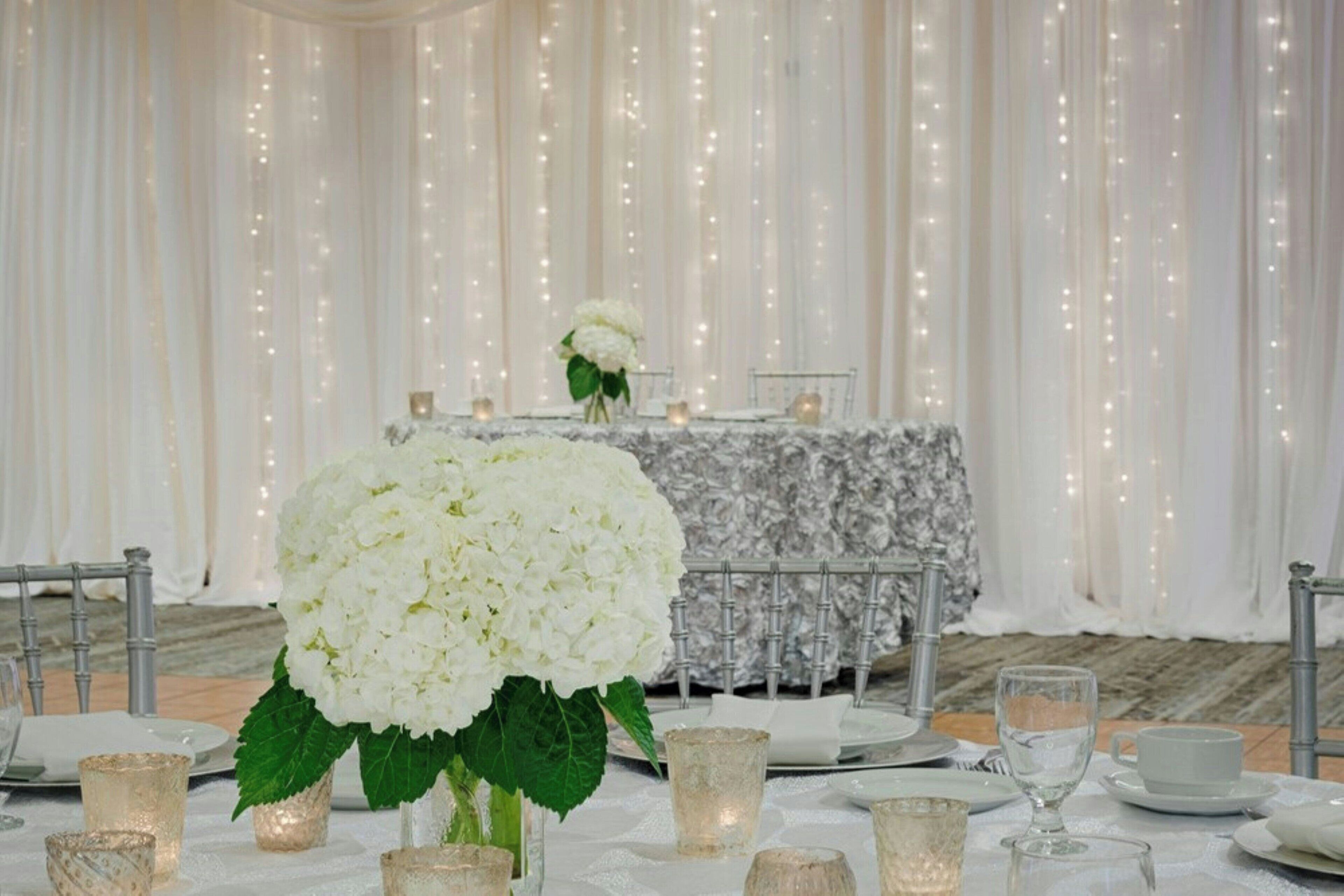 Una mesa dispuesta con platos blancos, vasos y un centro de mesa con flores blancas.