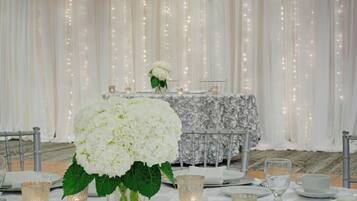 Una mesa dispuesta con platos blancos, vasos y un centro de mesa con flores blancas.