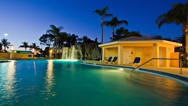 A swimming pool with a waterfall feature, lounge chairs, and palm trees. - Holiday Inn Port St. Lucie by IHG (Port Saint Lucie)