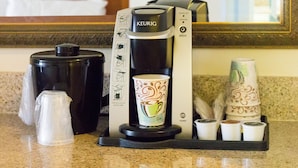 A coffee maker with instructions, a cup of coffee, and several disposable cups on a countertop. - Holiday Inn Port St. Lucie by IHG (Port Saint Lucie)