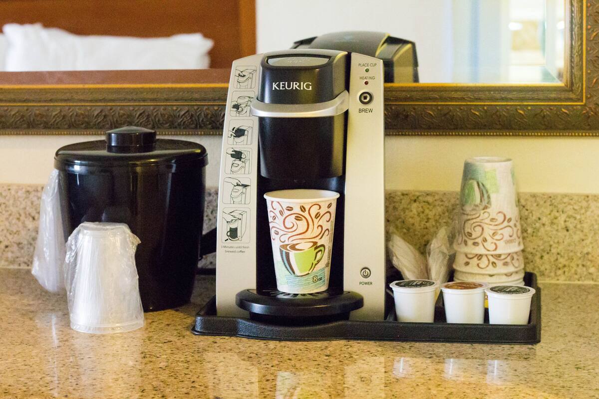 A coffee maker with instructions, a cup of coffee, and several disposable cups on a countertop.