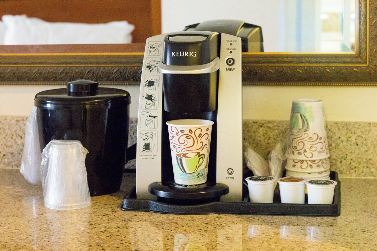A Keurig coffee maker with a drip tray, a coffee cup, and a stack of disposable coffee cups on a countertop.