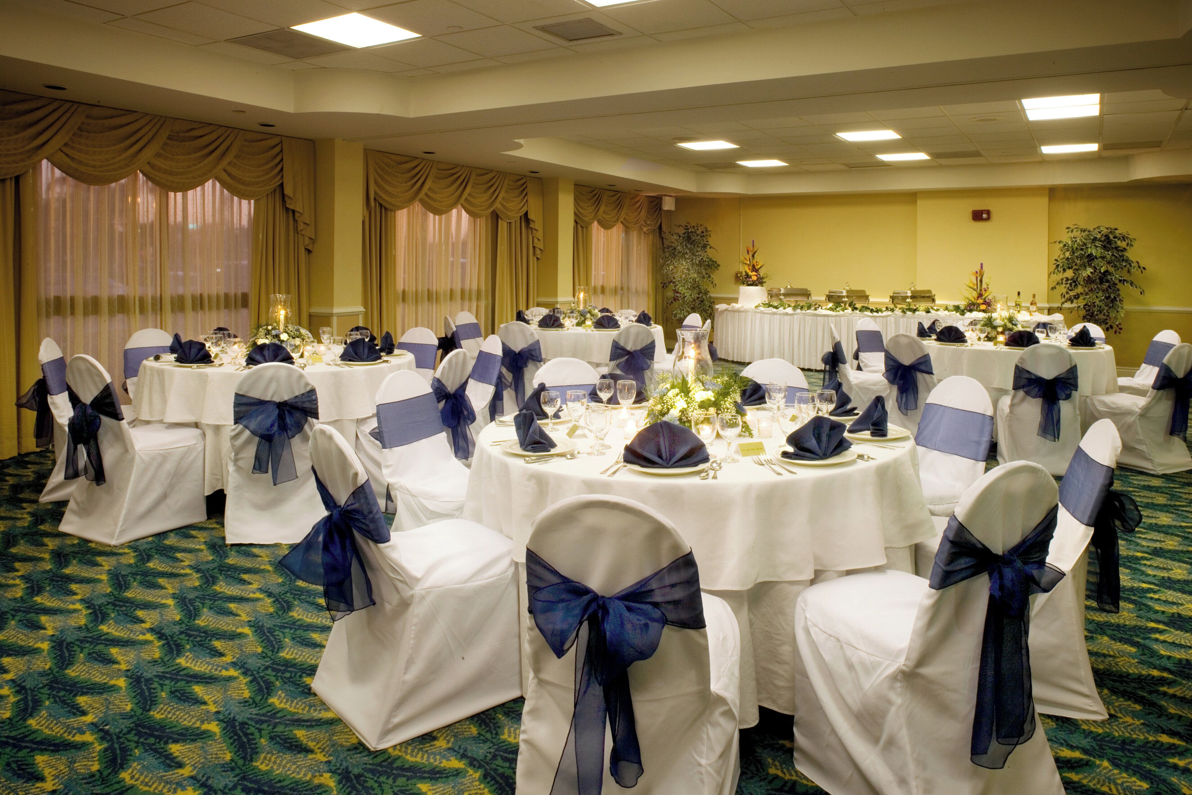 A banquet hall with round tables, white tablecloths, and chairs with blue sashes.
