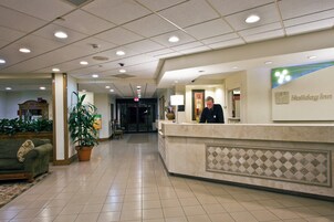 Un hall de hotel con una recepción, una planta, un sofá y suelo de baldosas.