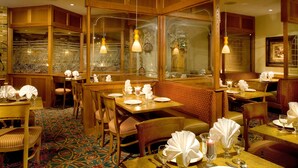 A restaurant with wooden booths, tables set with white tablecloths, and patterned carpet. - Holiday Inn Port St. Lucie by IHG (Port Saint Lucie)