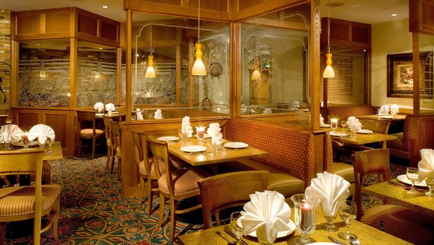 A restaurant with wooden booths, tables set with white tablecloths, and patterned carpet. - Holiday Inn Port St. Lucie by IHG (Port Saint Lucie)