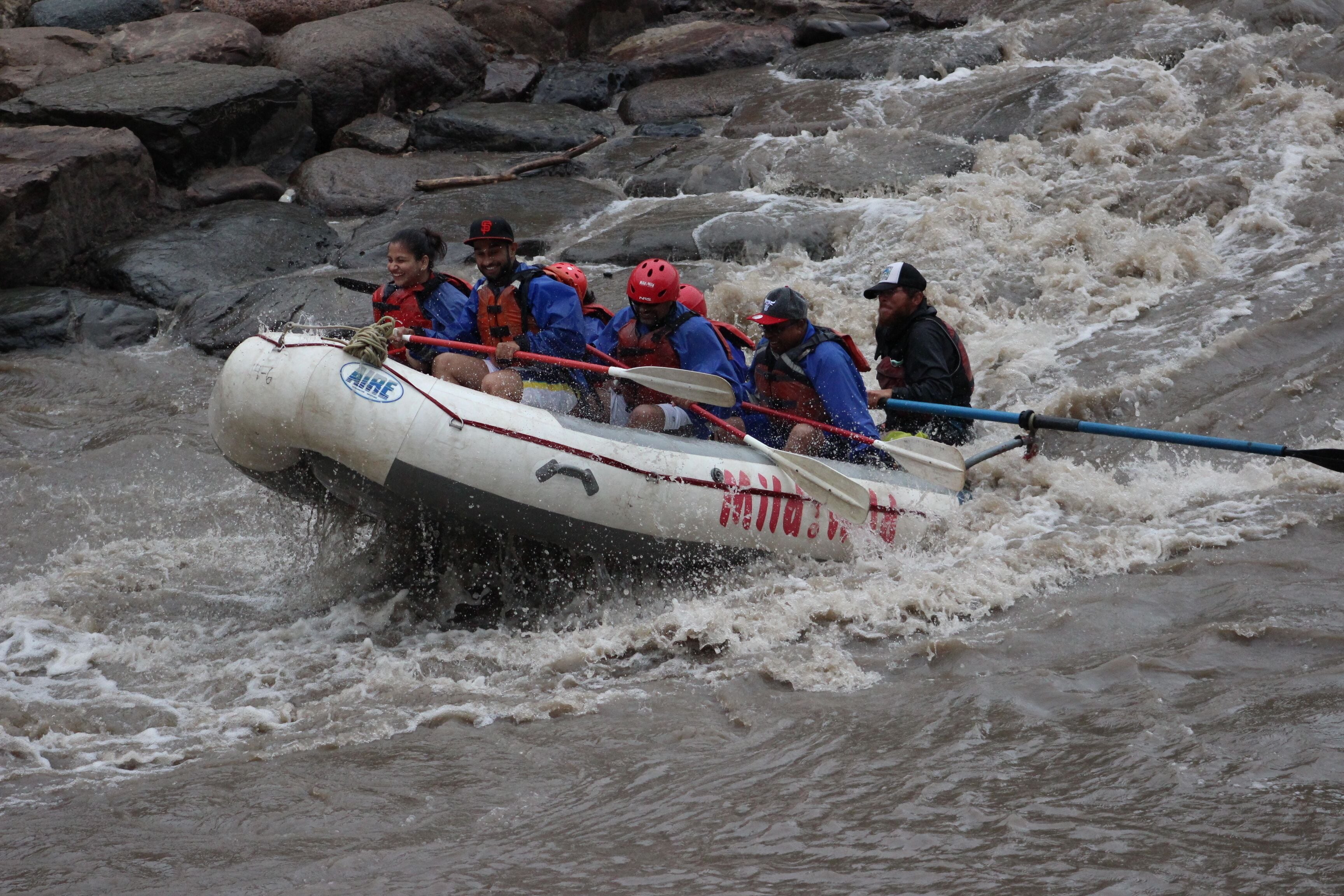 A group of people in a white inflatable raft navigating through a river with rapids.