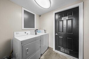 Un lavadero con lavadora y secadora Whirlpool, un espejo y una puerta con la leyenda 'Sala de máquinas'.