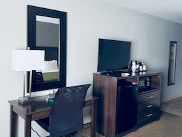 Habitación de hotel con escritorio de madera, una silla, televisor de pantalla plana, minibar y espejo.
