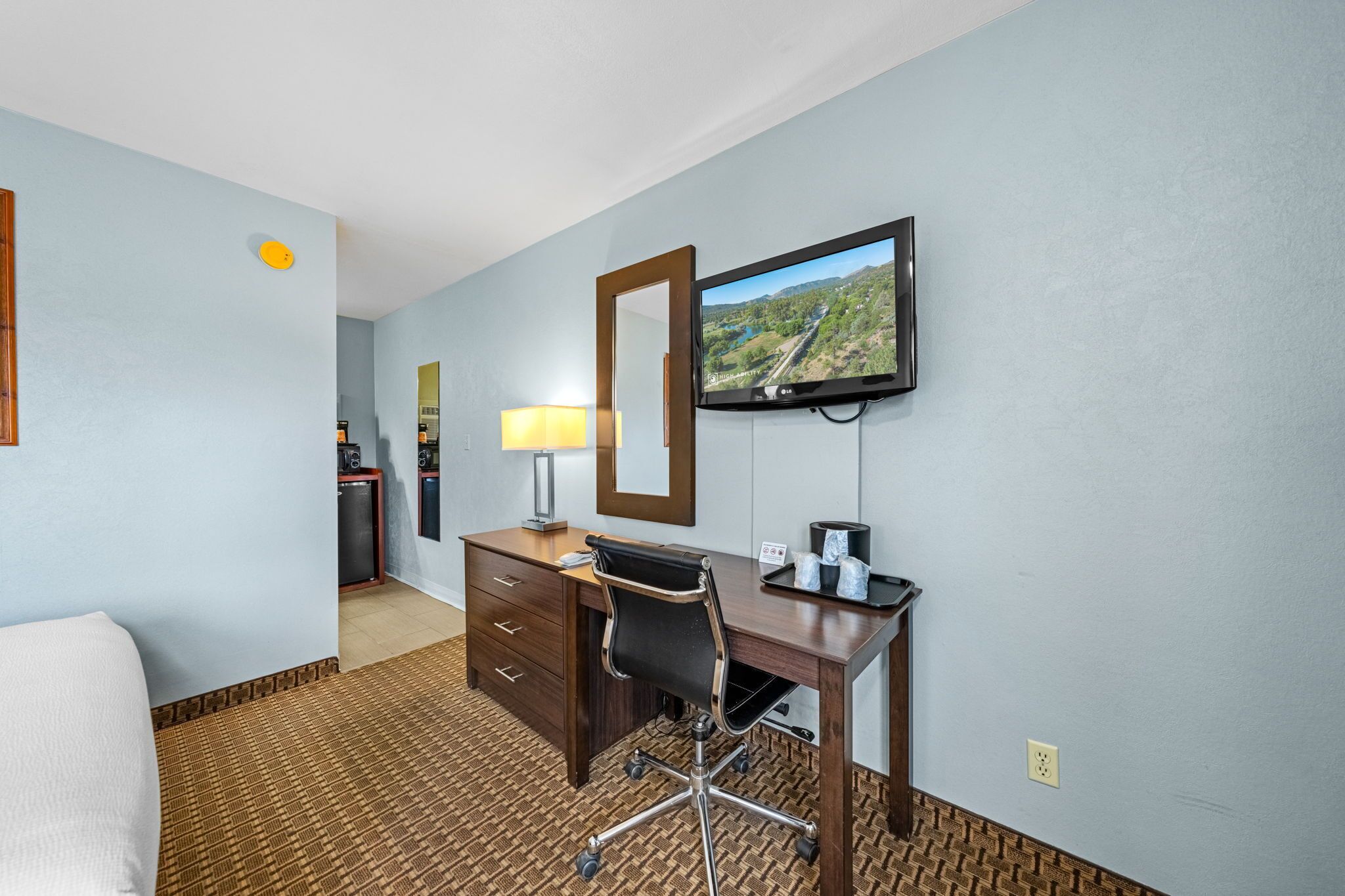 Een hotelkamer met een bed, een bureau met stoel, een televisie, een lamp en een spiegel.