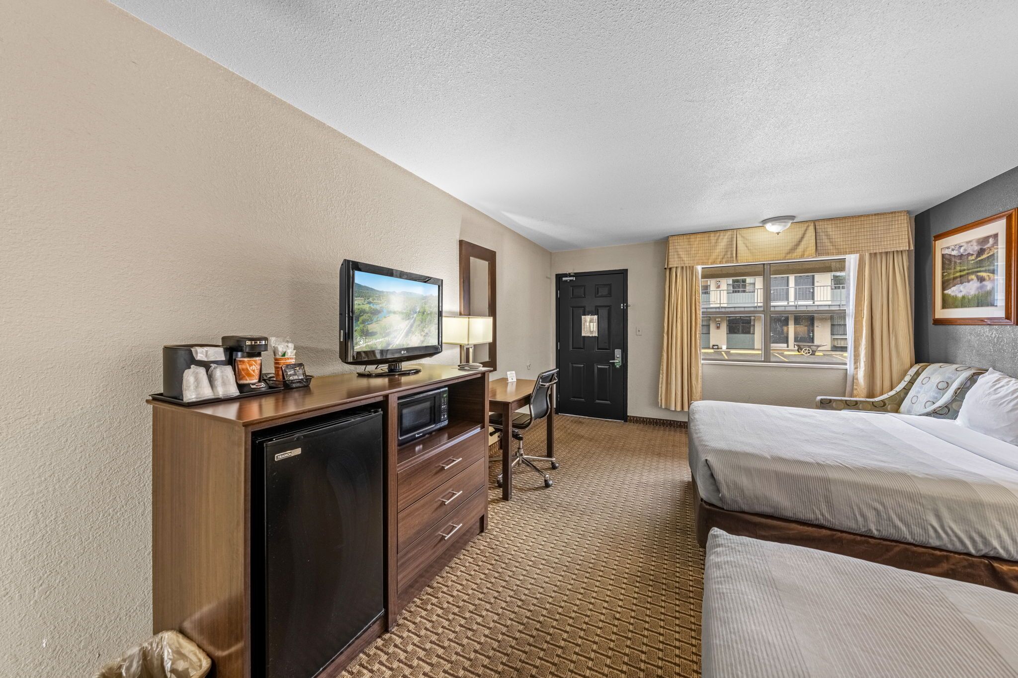 A hotel room with a bed, a desk with a computer, a television, and a minibar.
