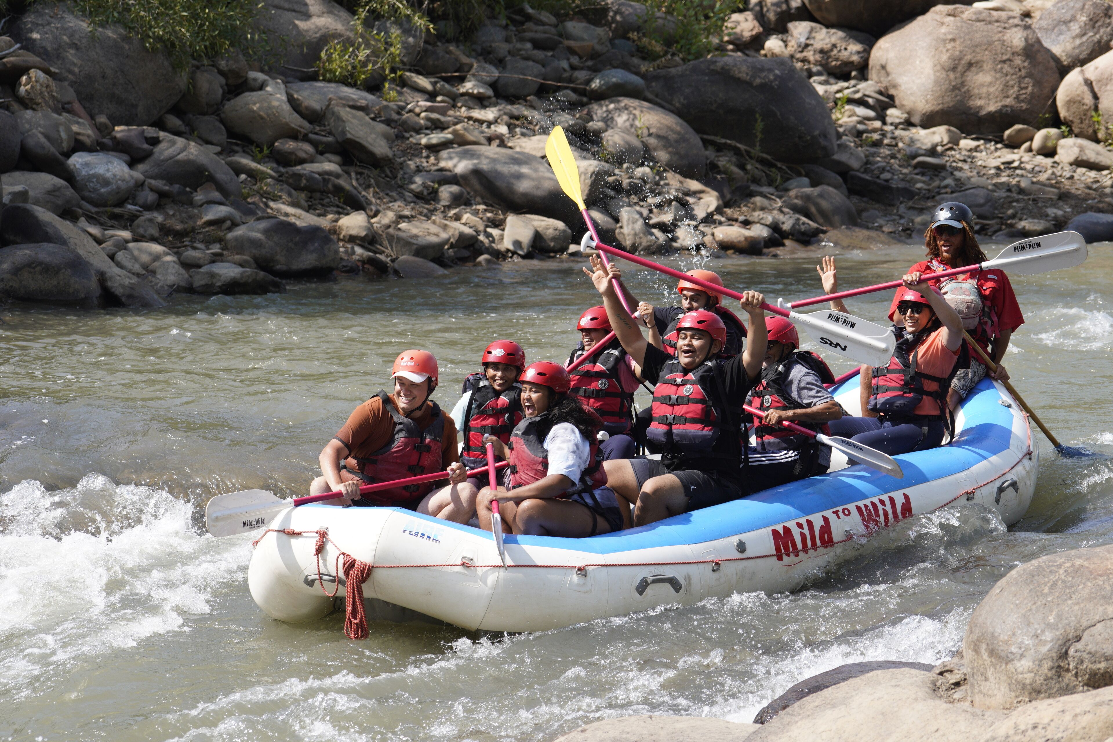 Eine Gruppe von Menschen in einem Floß, das einen Fluss mit Steinen und Felsen befahren.