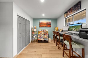 A home office with a desk, computer, and printer, a bookshelf, and a window with a view.