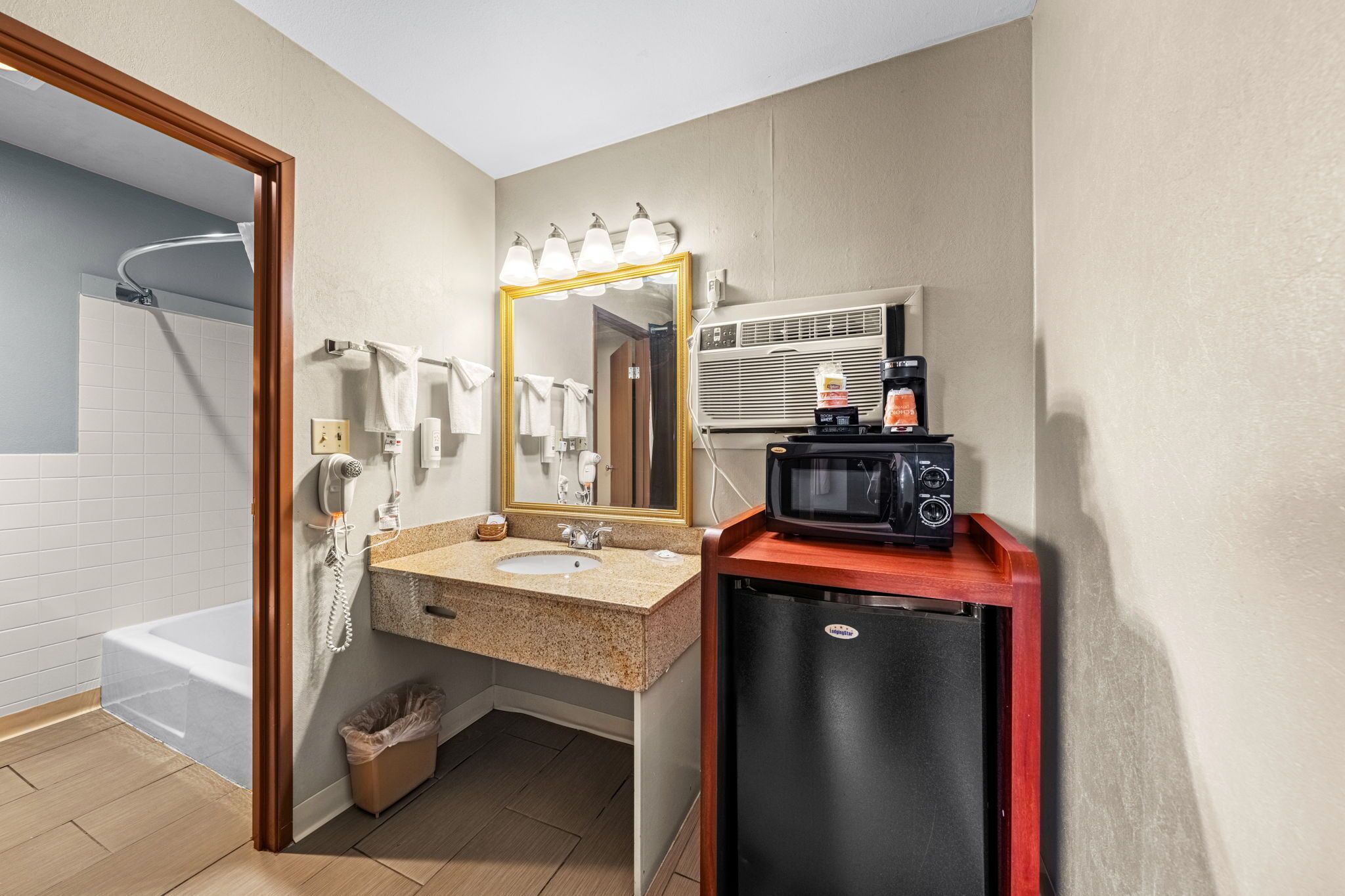 A bathroom with a sink, mirror, vanity, shower, and a small refrigerator.