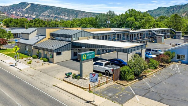 A modern building with a 'Quality Inn' sign, parking area, and a pedestrian crossing.