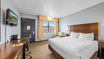 A hotel room with a large bed, a desk with a chair, a television mounted on the wall, and a window with curtains.