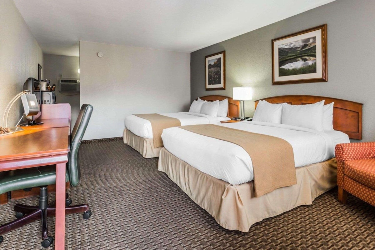 A hotel room with two beds, a desk, a chair, and a small table.