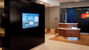 Un área de recepción con pantalla digital, mostrador de recepción y una planta en maceta.