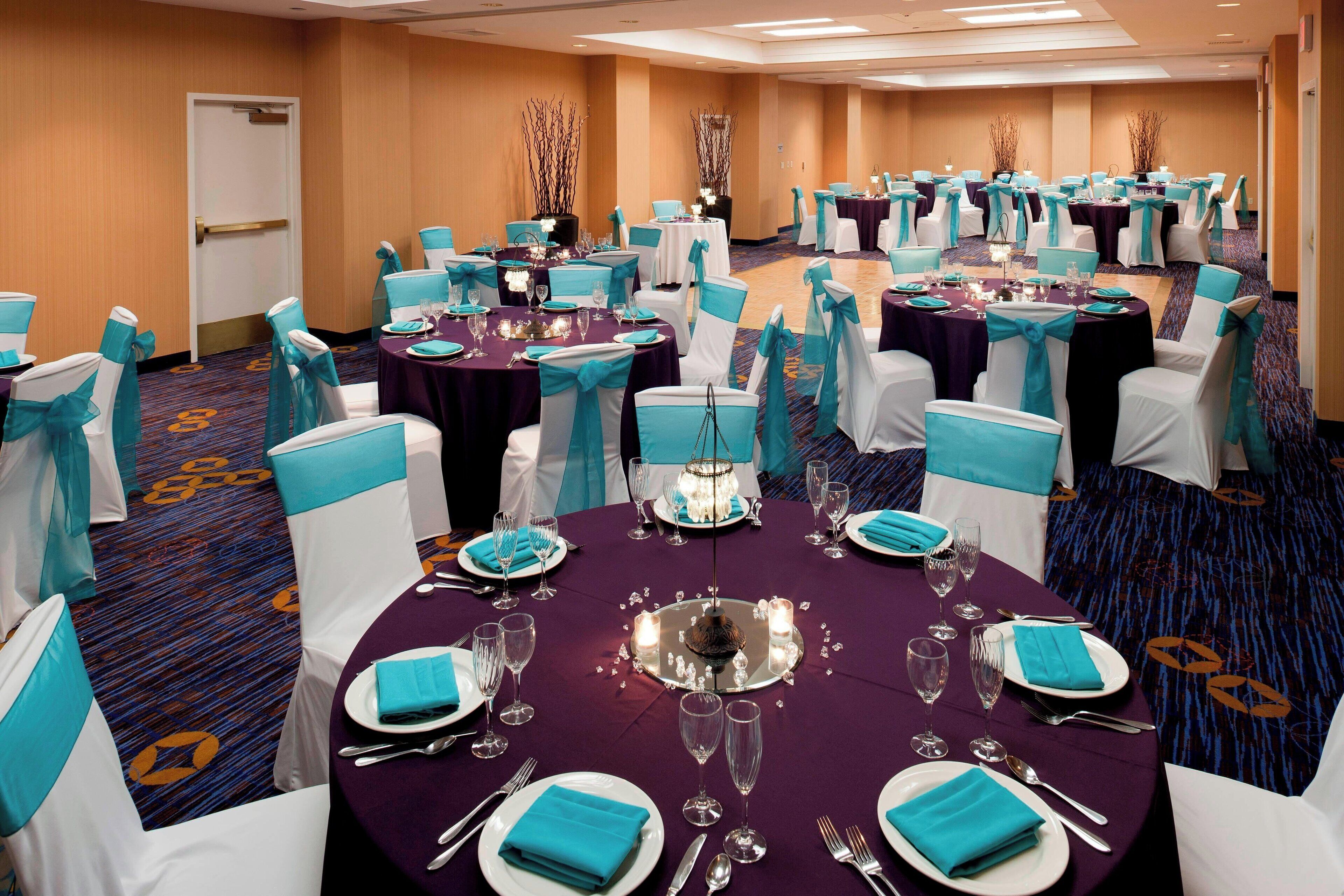 A banquet hall with round tables, white chairs, and teal accents.