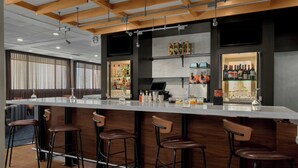 Una zona de bar moderna con una barra alargada, varios taburetes y una variedad de botellas y vasos en estanterías.