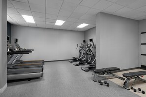 Une salle de sport équipée de tapis de course, de vélos elliptiques, d’un banc de musculation et d’haltères.