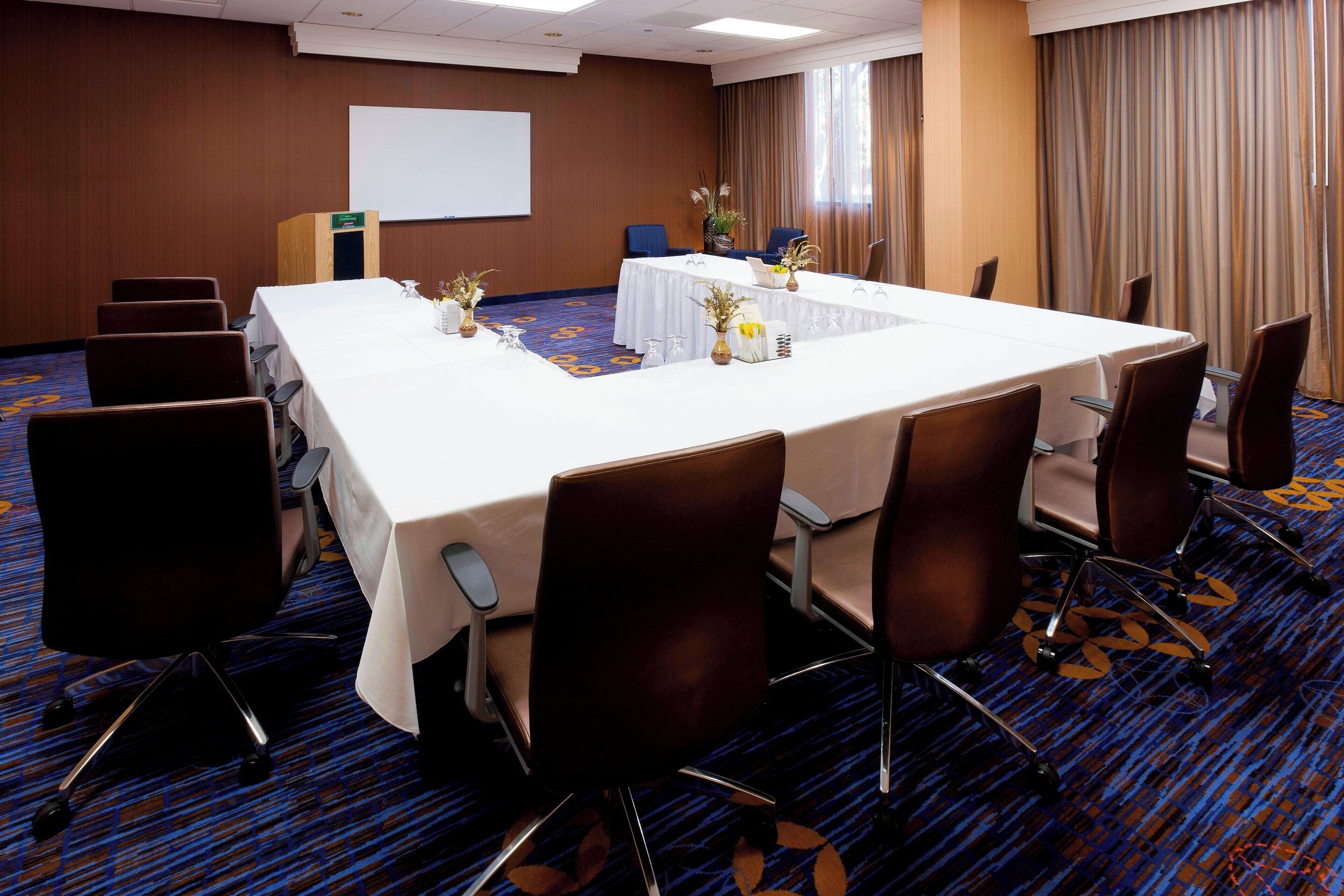 A conference room with a long table, chairs, a podium, and a projector screen.