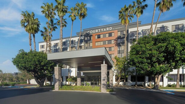 Un hotel moderno con un acceso cubierto, palmeras y un cielo azul despejado.
