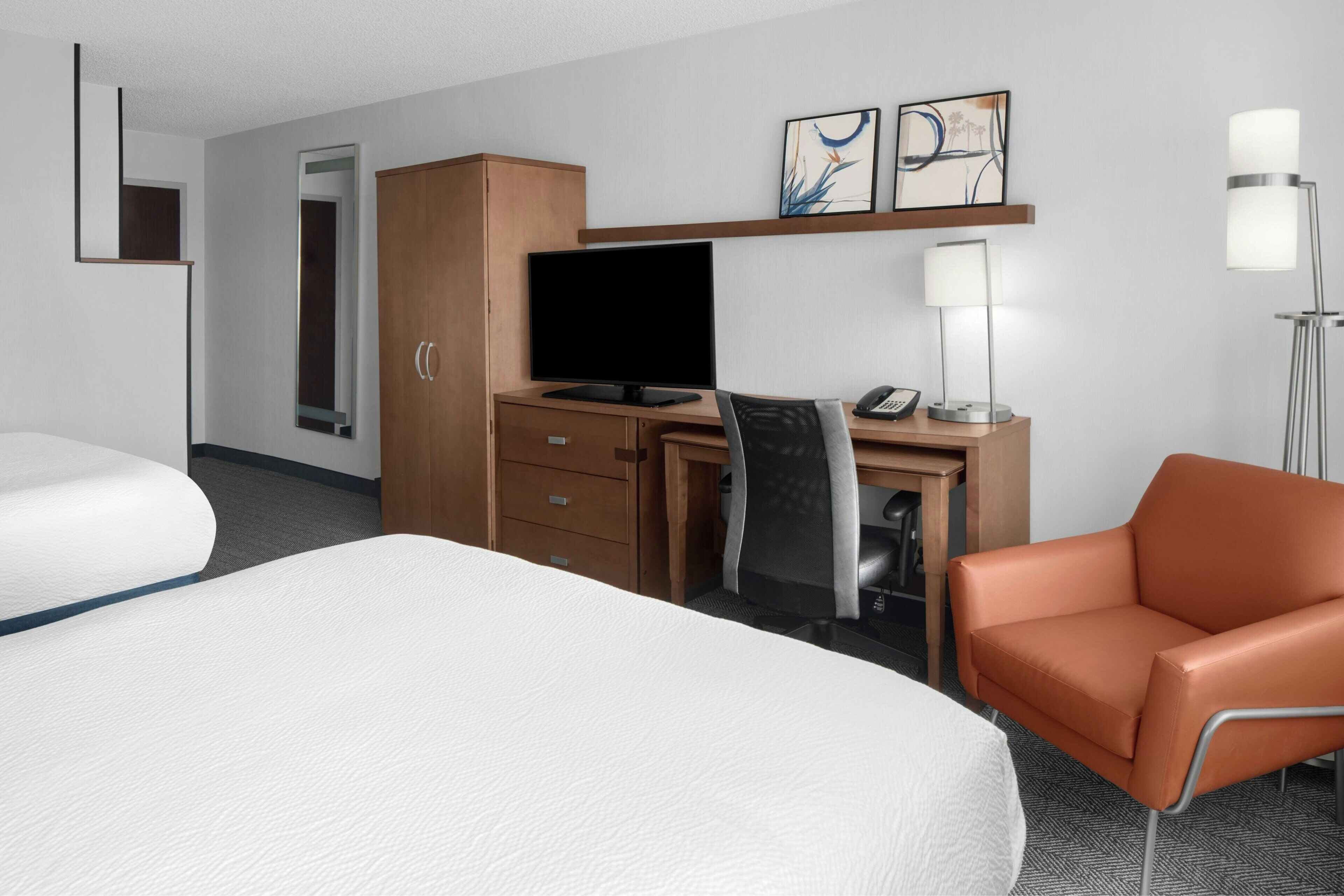 A hotel room with a bed, desk, chair, television, lamp, and artwork on the wall.