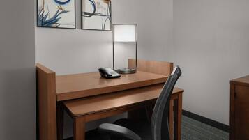 A hotel room with a wooden desk, a modern lamp, a telephone, and two abstract paintings on the wall.