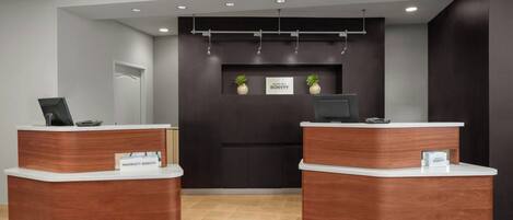 A reception area with two wooden reception desks, a dark wall with a sign, and a ceiling with recessed lighting.