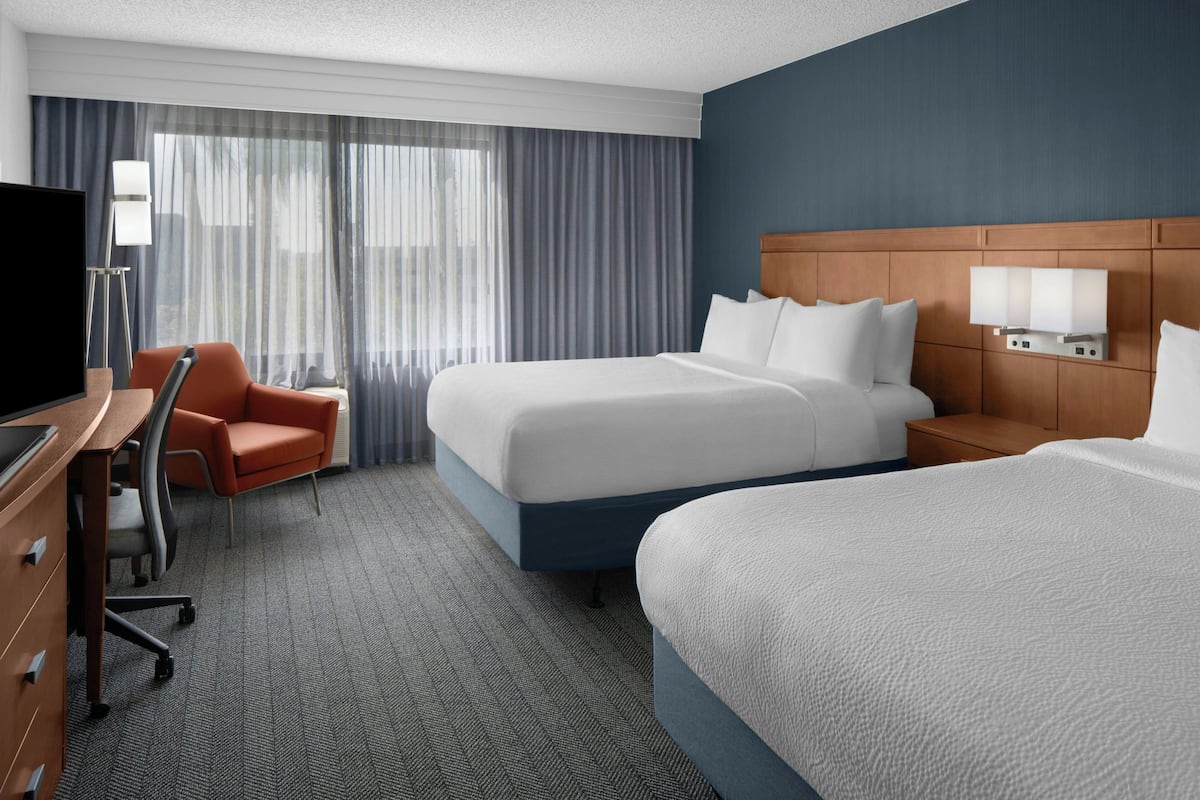 A hotel room with a large bed, a desk with a chair, a TV, and a window with curtains.