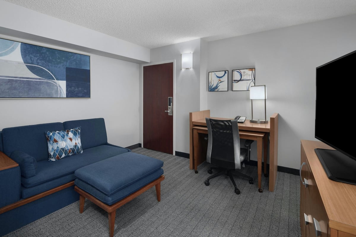 A hotel room with a blue sofa, a desk with a chair, a television, and artwork on the walls.