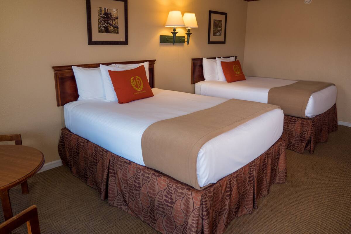 Una habitación de hotel con dos camas, una mesa de comedor y una lámpara de pared.