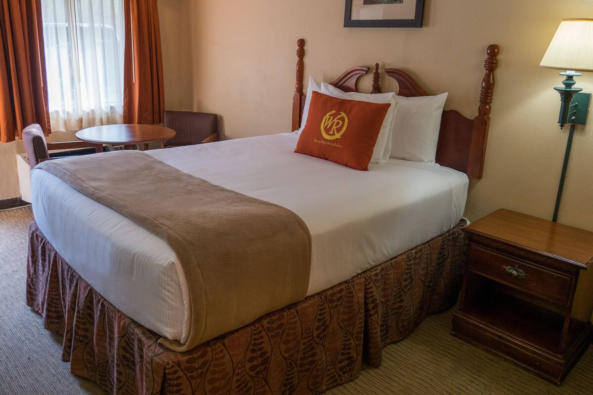 Una habitación de hotel con una cama grande, un cabecero de madera, una mesita de noche, una silla y una lámpara.