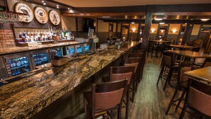 A bar area with a granite countertop, multiple liquor bottles, and a selection of glasses. There are wooden chairs and tables arranged for seating.