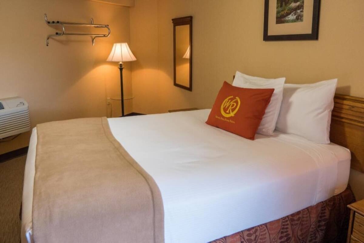 Habitación de hotel con cama, lámpara de noche, espejo y aire acondicionado instalado en la pared.