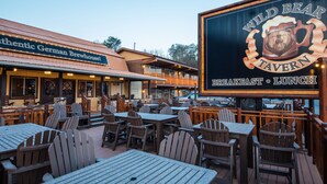 An outdoor seating area with tables and chairs, a sign for Wild Bear Tavern, and a building with a sign for Authentic German Brewhouse.