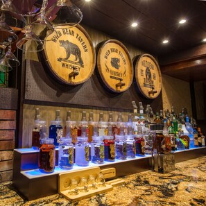 Een barruimte met houten vaten met de tekst 'Wild Bear Tavern Whiskey' en verschillende drankflessen.
