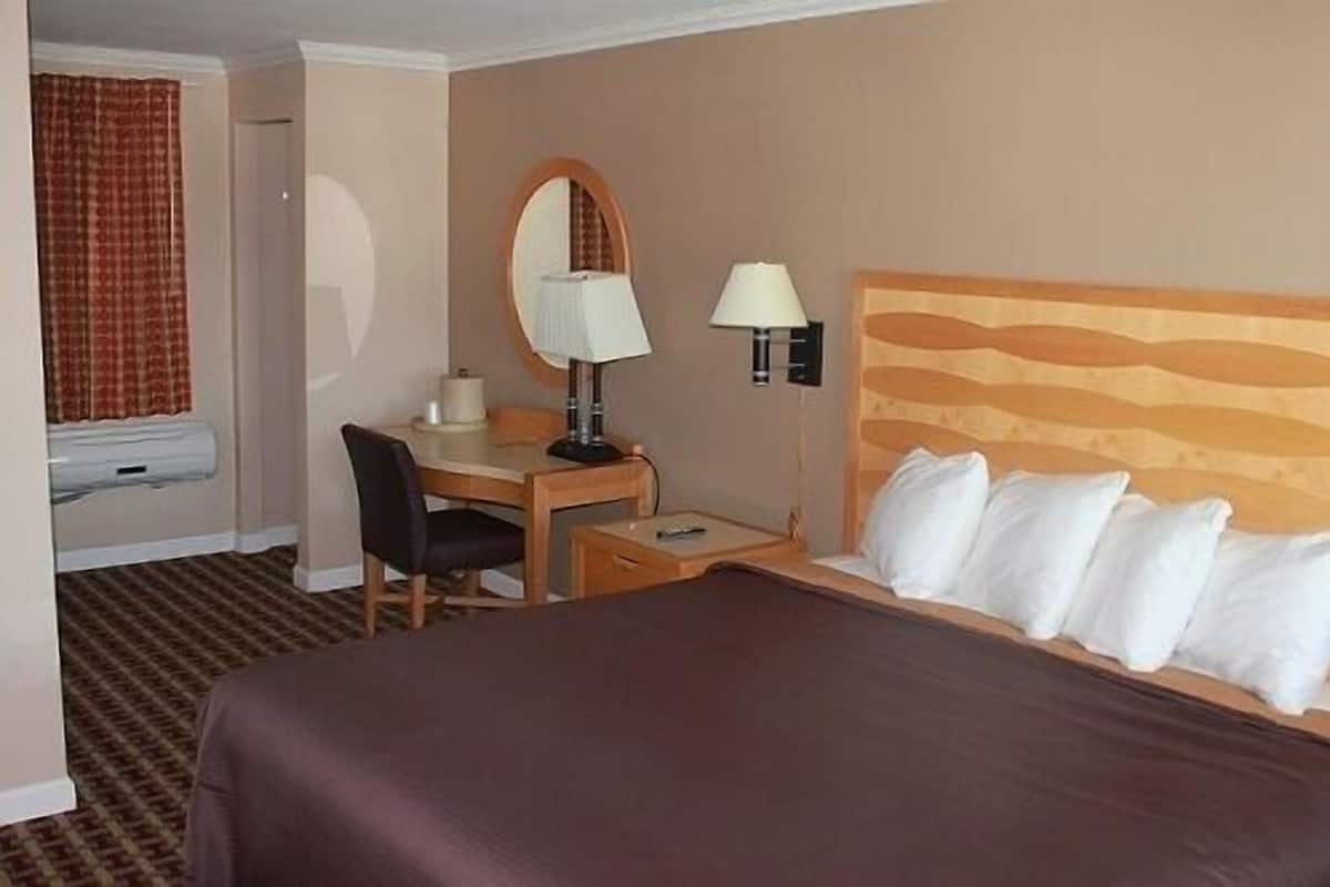 A hotel room with a bed, a desk with a chair, a lamp, and a window with curtains.