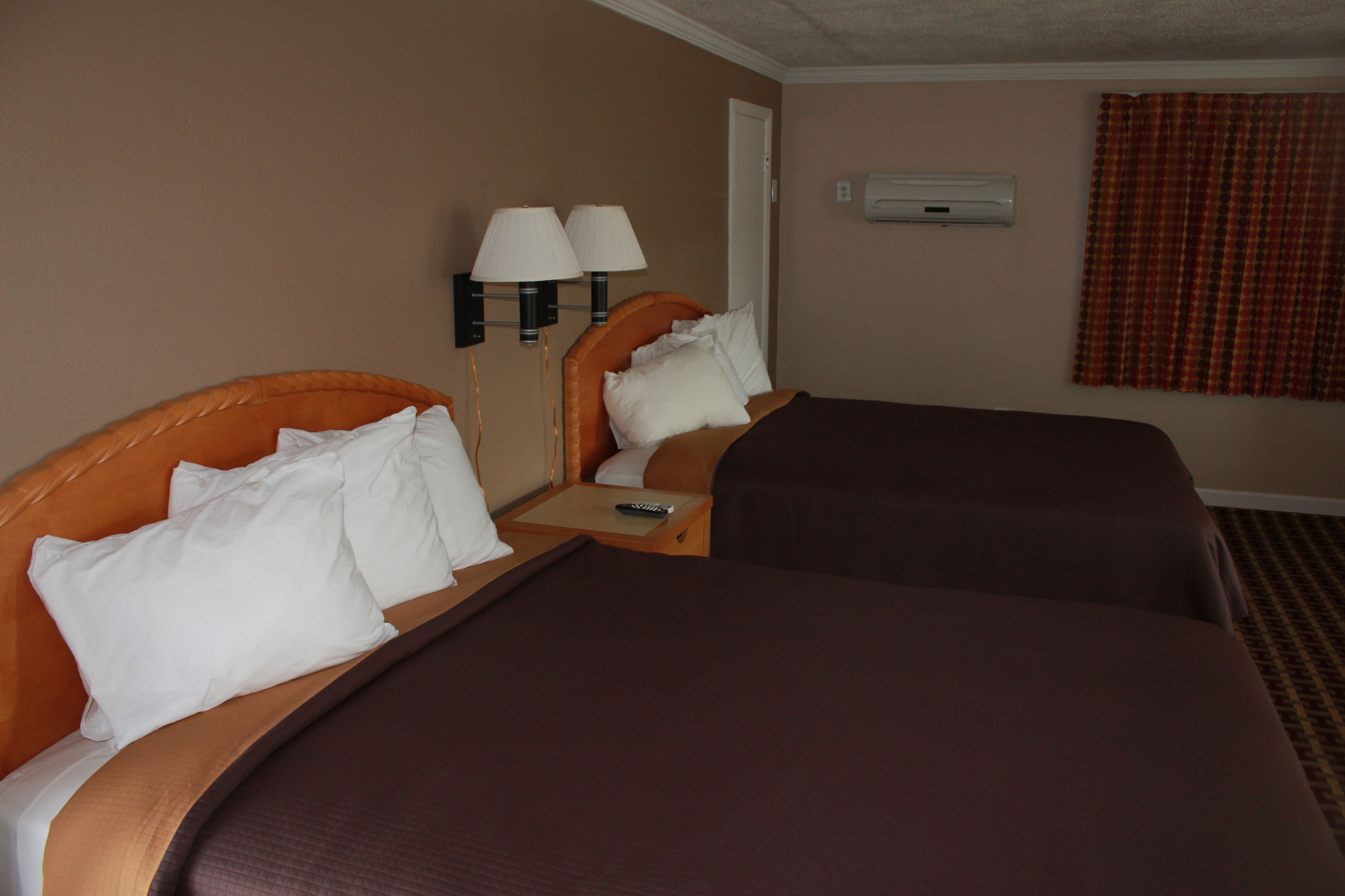Quarto de hotel com duas camas, cada uma com cabeceira, mesa de cabeceira com controle remoto e ar condicionado fixado na parede.