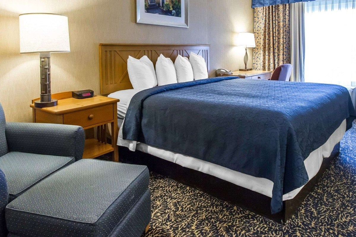 A hotel room with a large bed, a desk, a chair, and a nightstand.