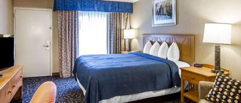 A hotel room with a large bed, a desk with a lamp, a chair, and a television.