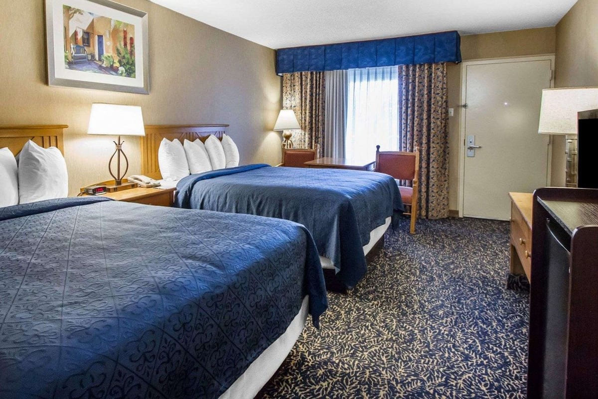 A hotel room with two beds, a desk, a chair, a TV, and a painting on the wall.