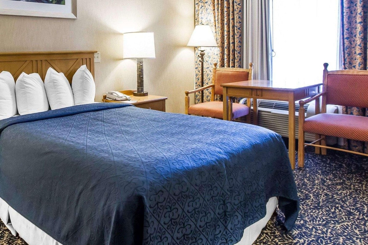 A hotel room with a large bed, a desk with a chair, a lamp, and a painting on the wall.