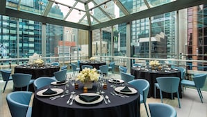 A rooftop dining area with round tables set for four, each with a black tablecloth, white plates, and blue chairs.