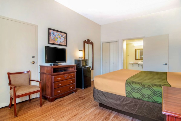 Une chambre d’hôtel avec un lit, une commode en bois, une télévision et un miroir.