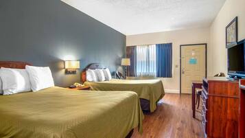 A hotel room with two beds, a desk, a TV, and a door.