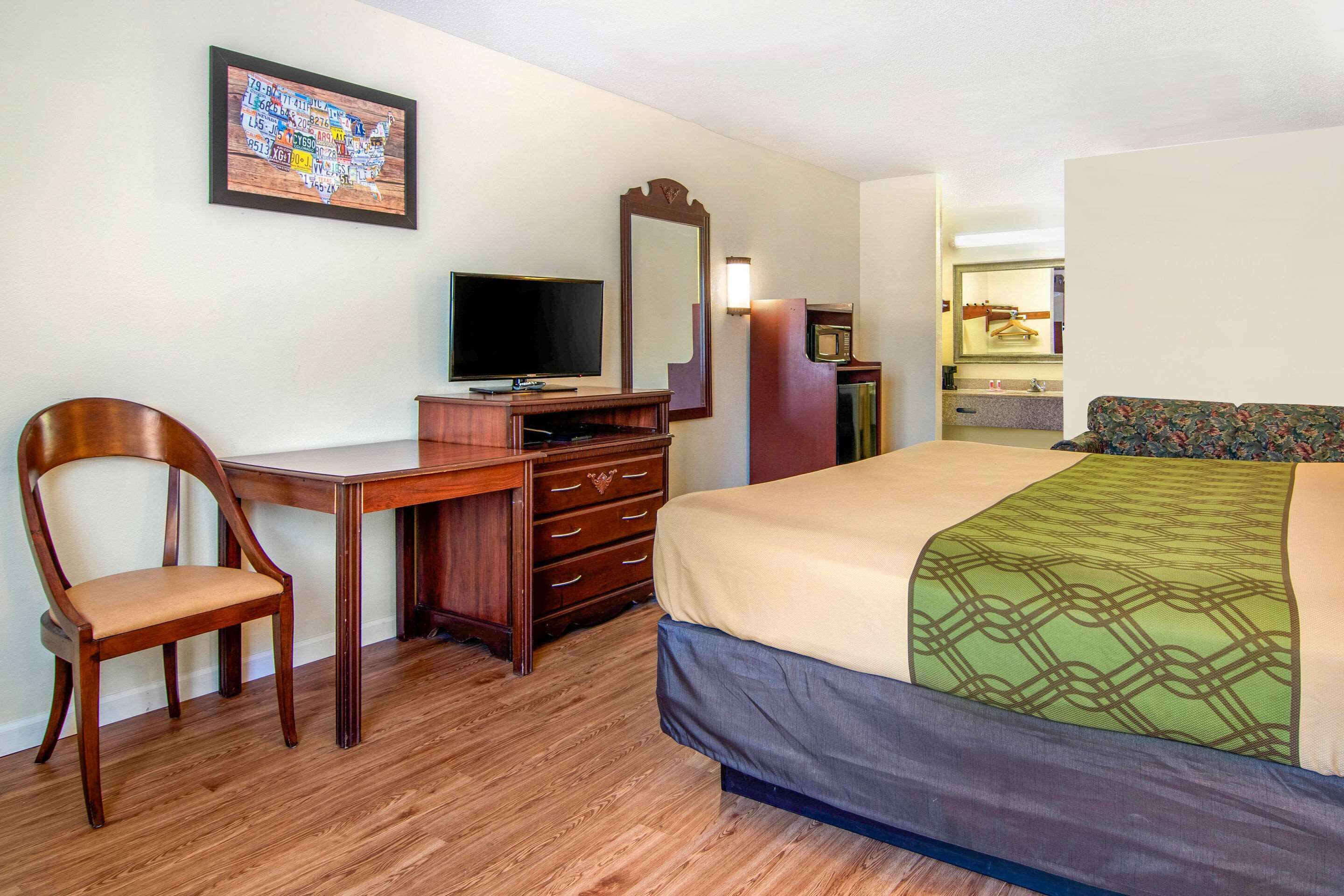 Une chambre d’hôtel avec un bureau en bois, une télévision, un lit avec une couvre-lit à motifs, un miroir et une commode.
